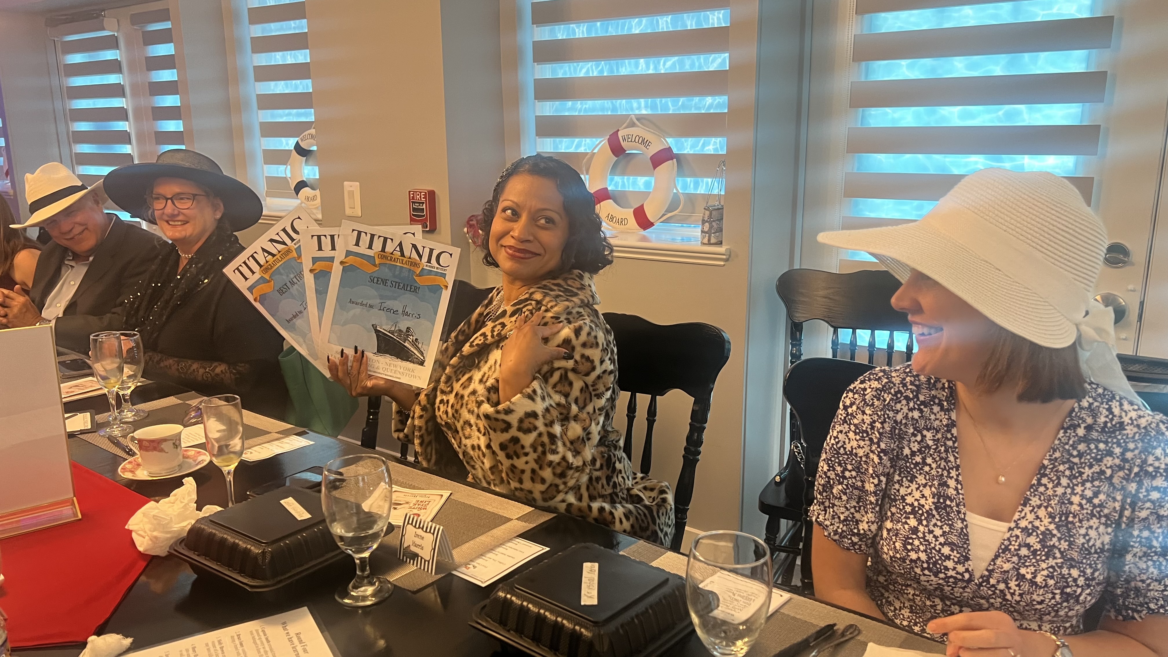 Woman seated with others a Titanic Murder Mystery holding awards she's won