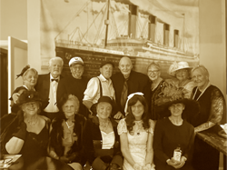 A group of people dressed for the early 1900's standing in front of a wall mural of the Titanic Ocean Liner