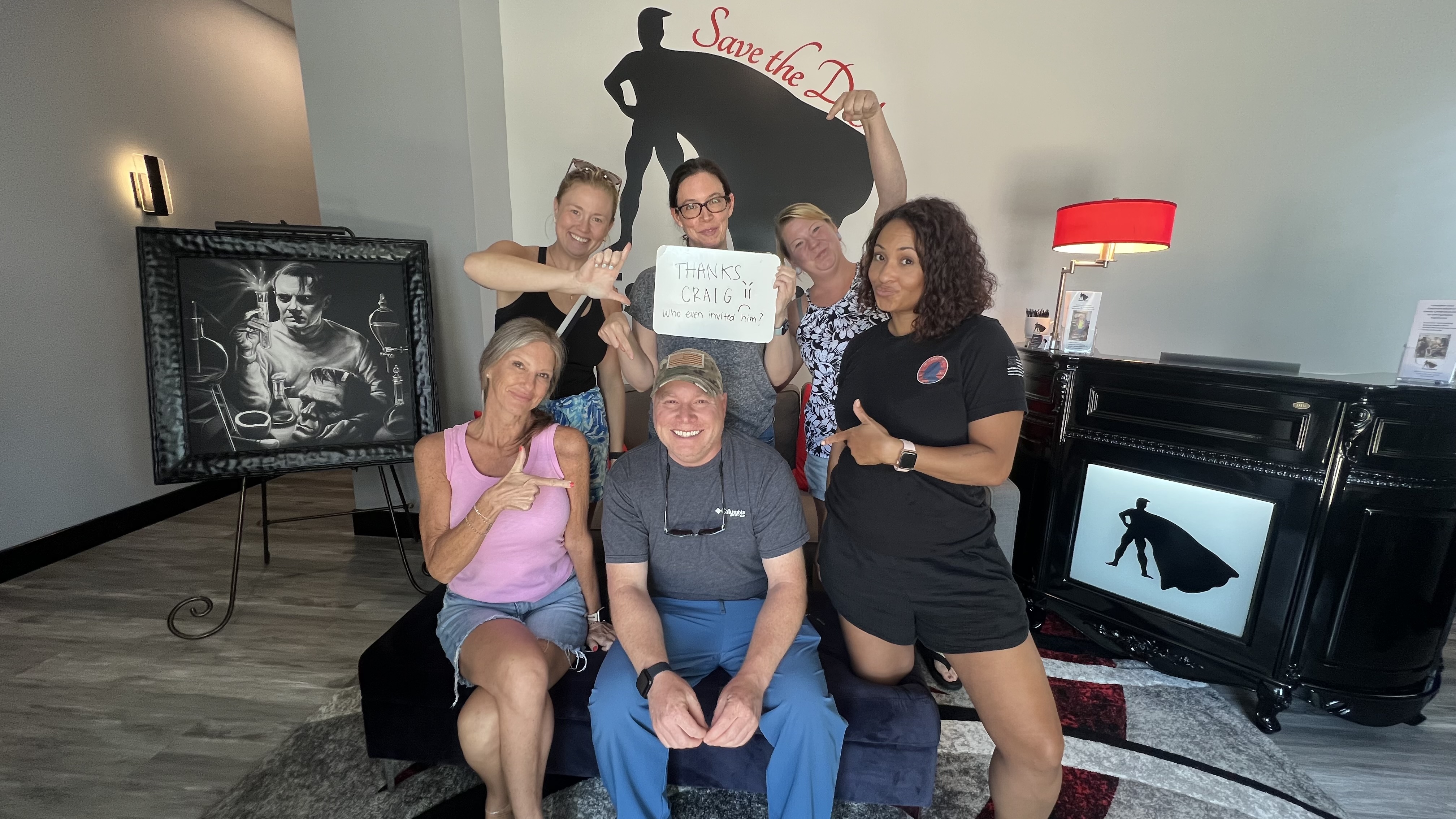 One man surrounded by 5 women pointing to him with a sign that says Thanks Craig Who invited you anyway