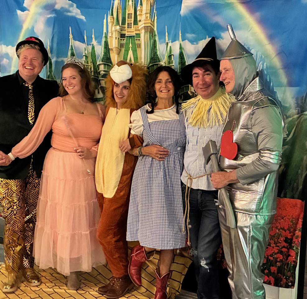 A young girl dressed in a blue gingham dress, a scarecrow, a lion, and a man made of tin with a funnel on his head