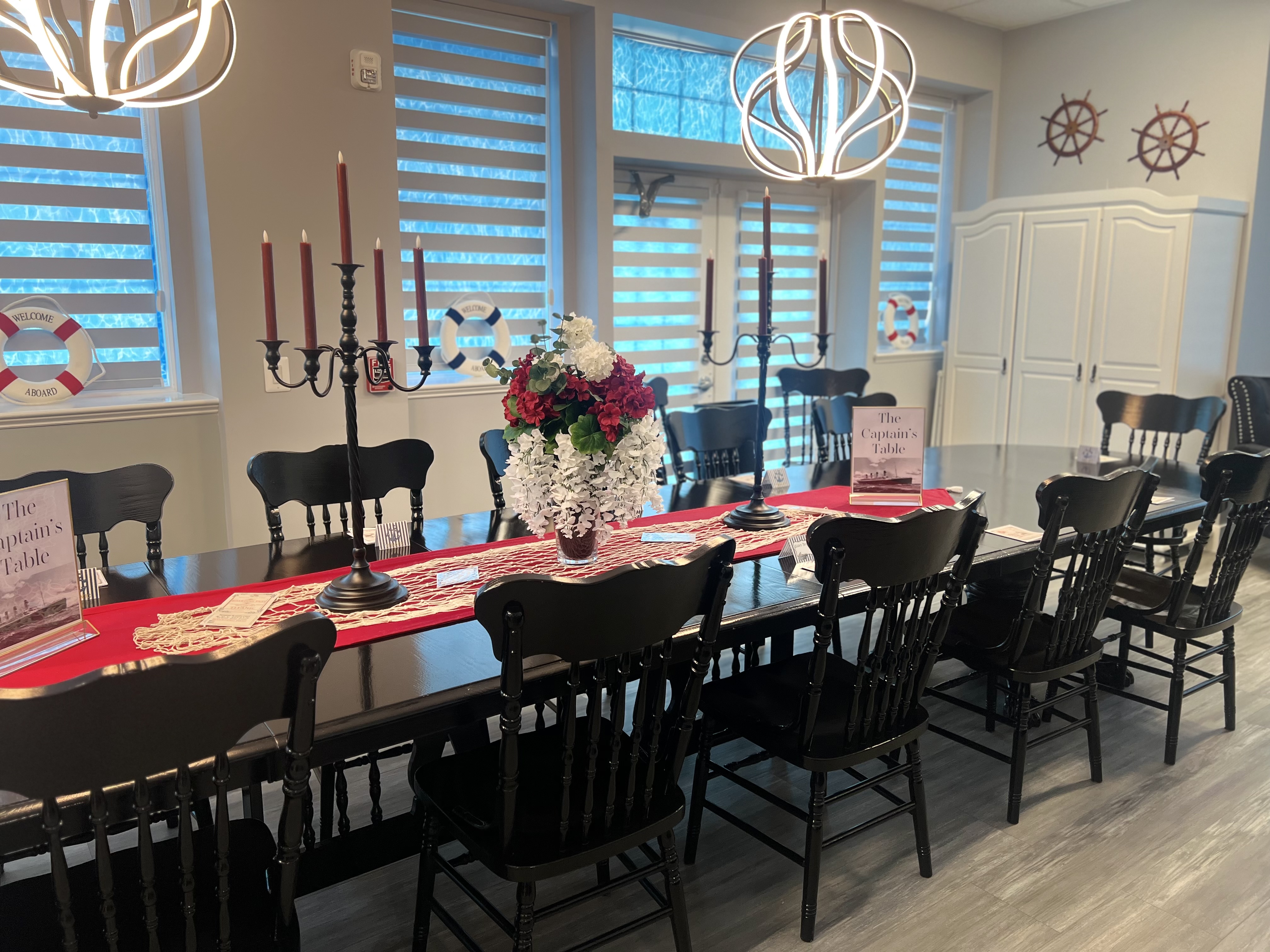 a banquet room with a large black laquered table with life perservers, netting, captain's table sign all decorated for a Titanic Murder Mystery